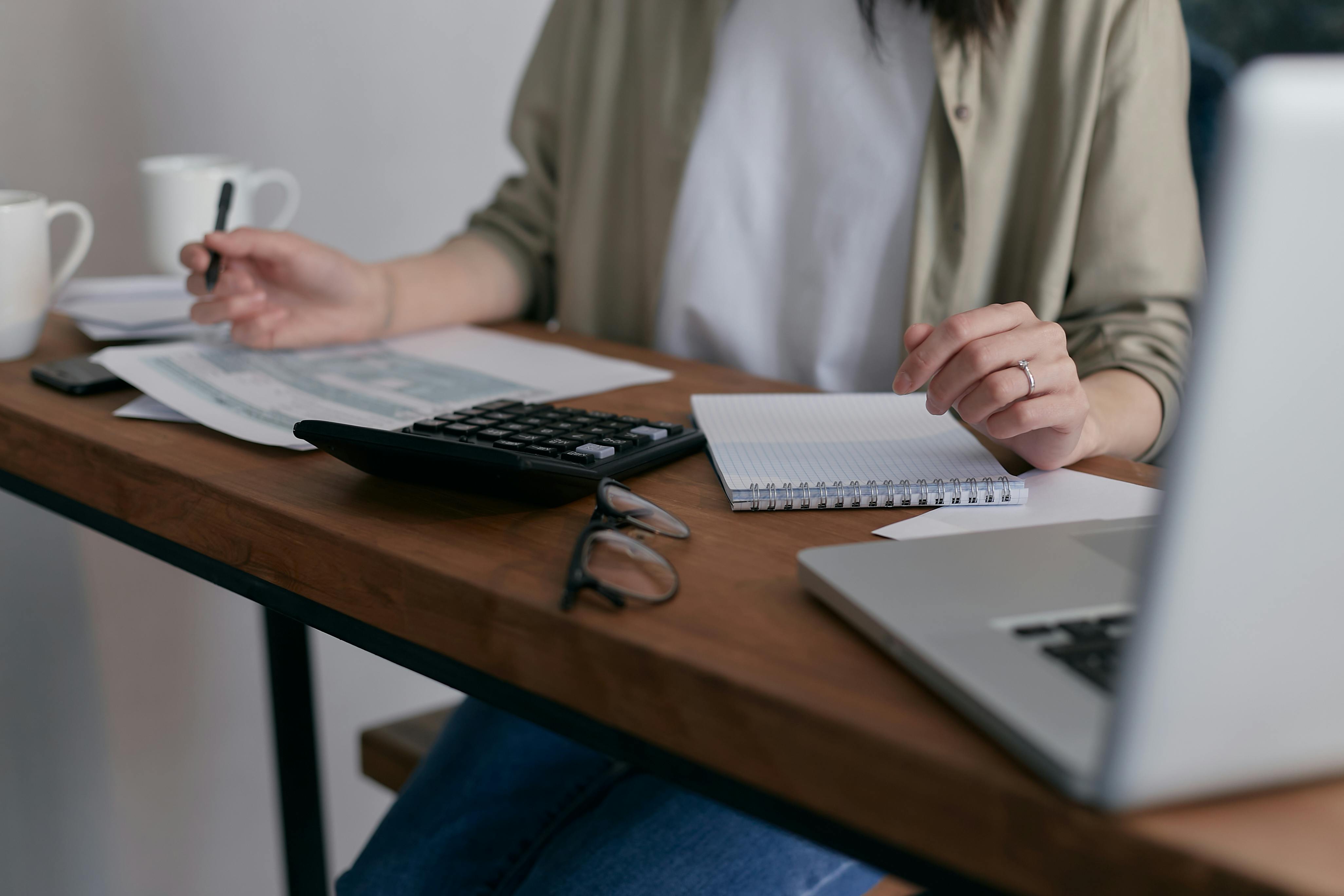 Person holding a pen while sitting at a desk with papers and a calculator on it